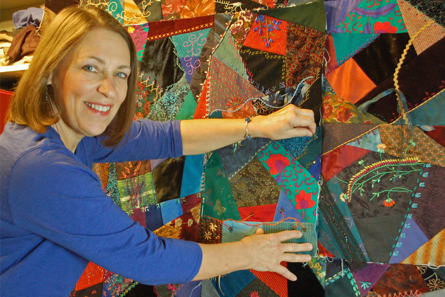 Jan Bjorkman looks to the camera while holding a piece of a Crazy Quilt in place.